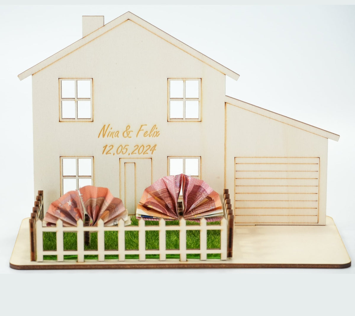 Holzhaus-Geldgeschenk mit personalisierter Gravur „Nina & Felix" samt Hochzeitsdatum, Geldschein-Fächer im Garten mit Rasen