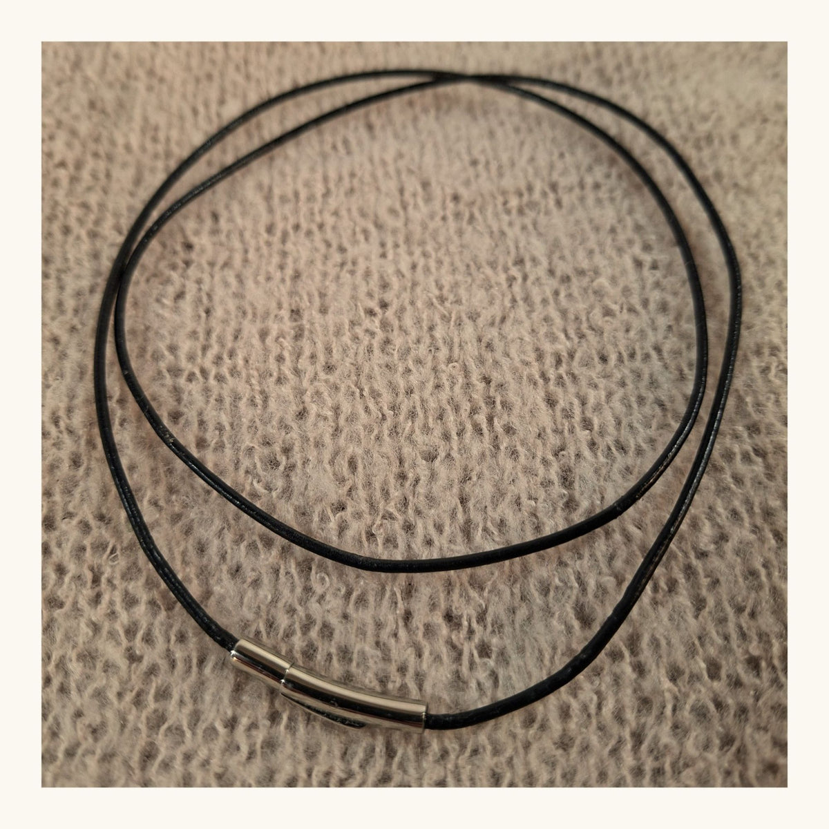 Schwarzes Lederband mit Edelstahl-Hebelverschluss, als Ring gelegt auf rosa Strickstoff